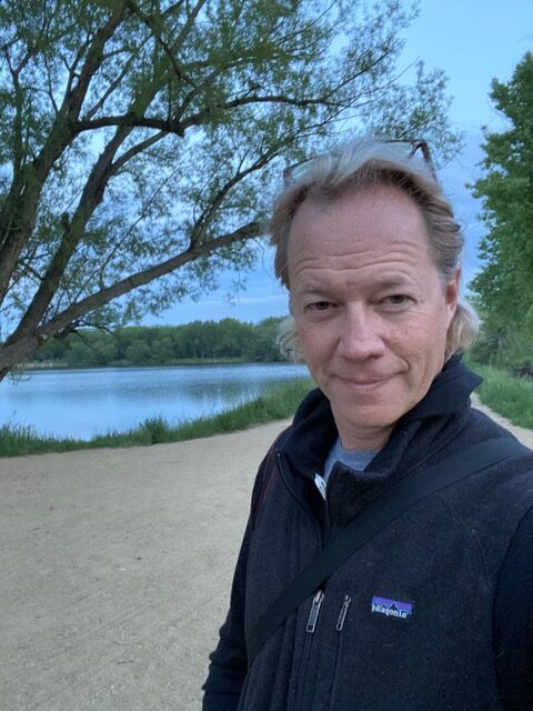 A photo of Brad McLain standing with water and trees in the background.